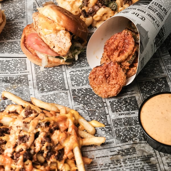 Assortment of burgers, loaded fries, mac and cheese, fried pickles, and dipping sauce on newspaper.