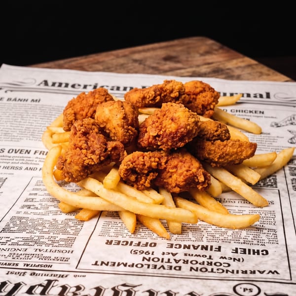 Crispy fried chicken pieces and golden french fries served on newspaper on a wooden board.