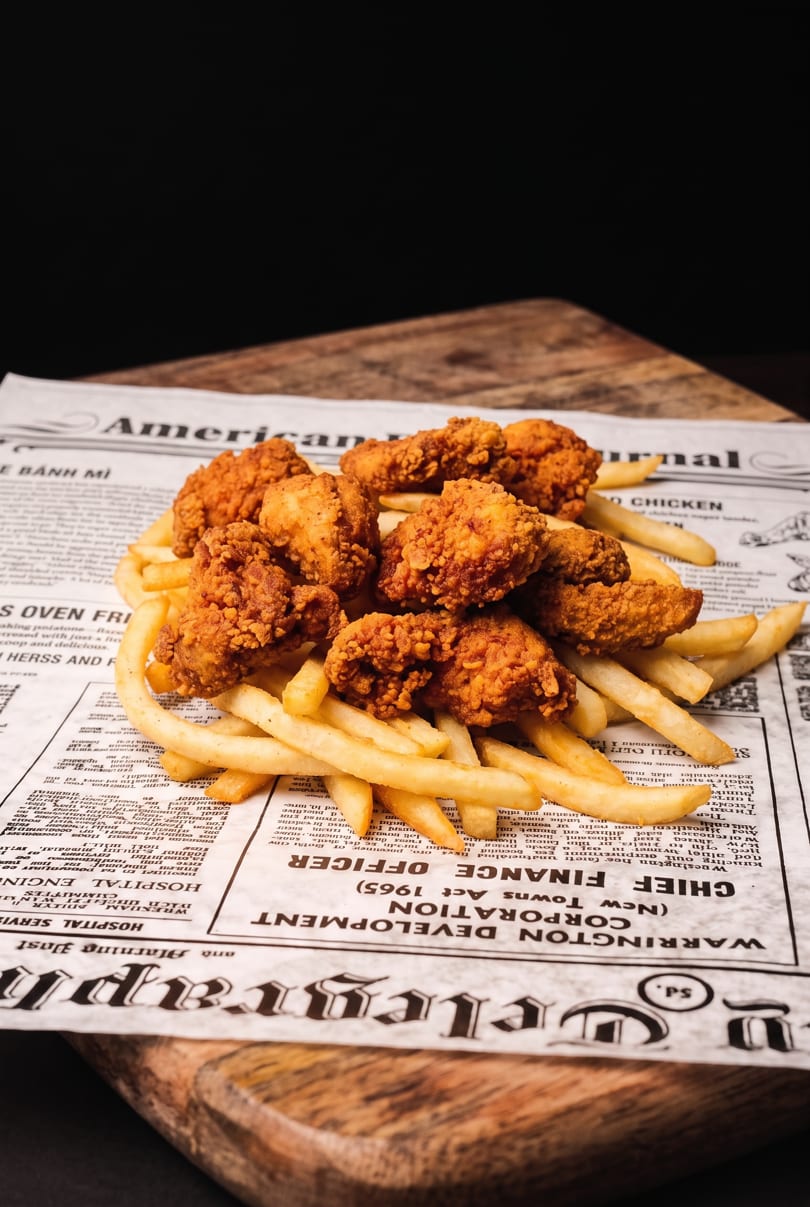 Crispy fried chicken pieces and golden french fries served on newspaper on a wooden board.