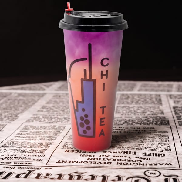 Gradient purple and orange bubble tea cup with 'CHI TEA' logo on a newspaper.