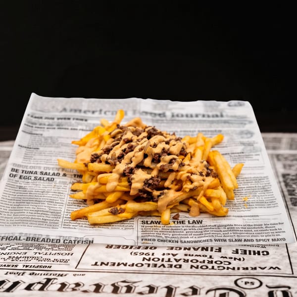 Loaded french fries with cheese sauce and ground beef, served on newspaper print.