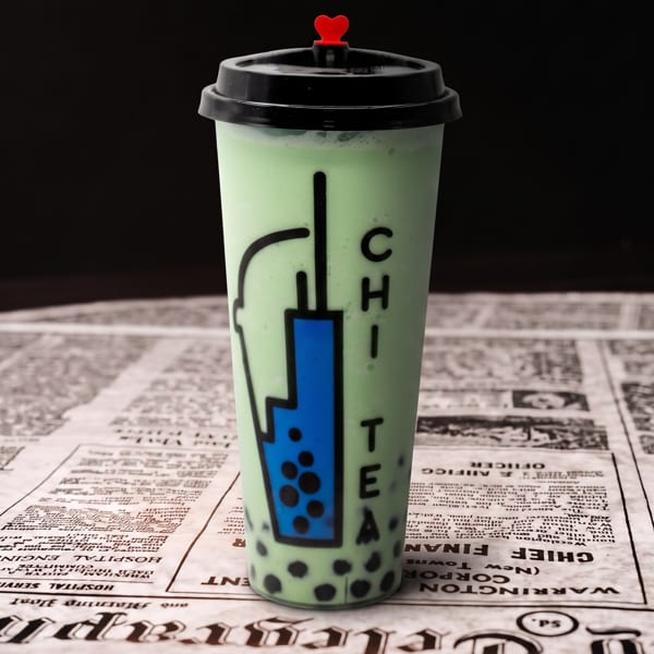 Green bubble tea with a 'CHI TEA' logo and red heart stopper on a newspaper.