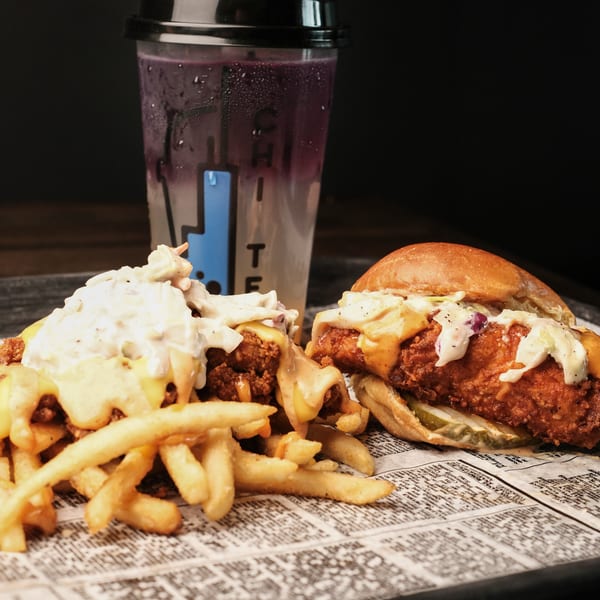 A fried chicken sandwich, loaded fries, and a purple drink on a tray with newspaper lining.