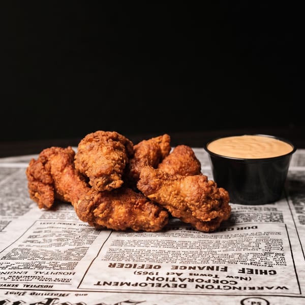 Golden-brown fried chicken drumettes and wings with dipping sauce on newspaper.