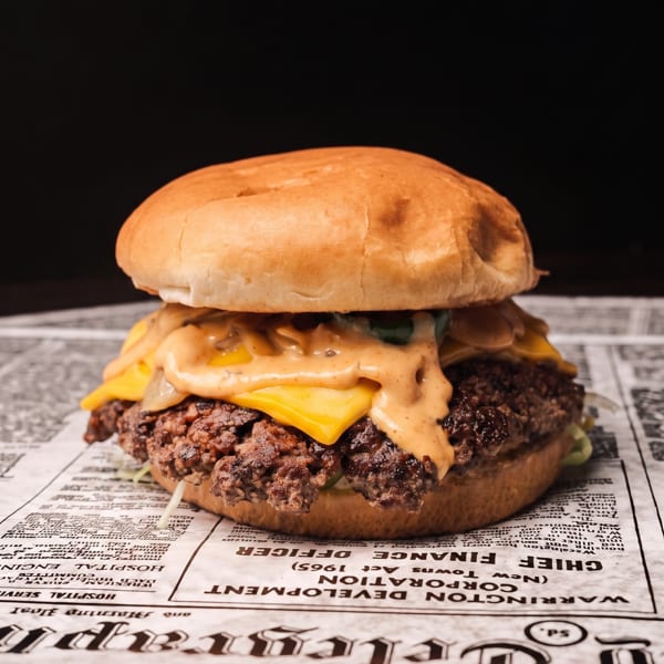 Juicy burger with melted cheese and special sauce on a newspaper, against a dark background.