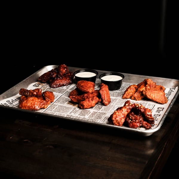 A metal tray with five piles of chicken wings and two small cups of dipping sauce.