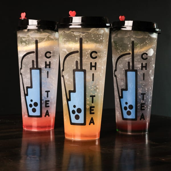 Three Chi Tea drinks in clear cups with red, orange, and purple liquid on a dark table.